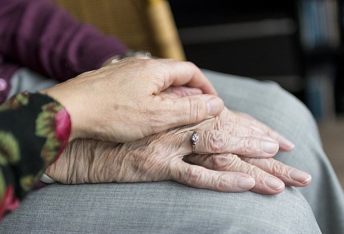 Eine Hand berührt eine Hand einer Seniorin